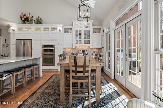 dining area with a chandelier, light wood-style flooring, french doors, and vaulted ceiling