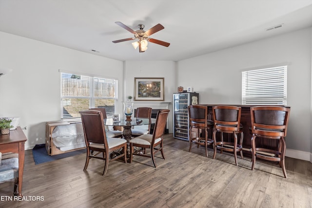 dining area featuring dark wood-type flooring, beverage cooler, ceiling fan, and indoor bar