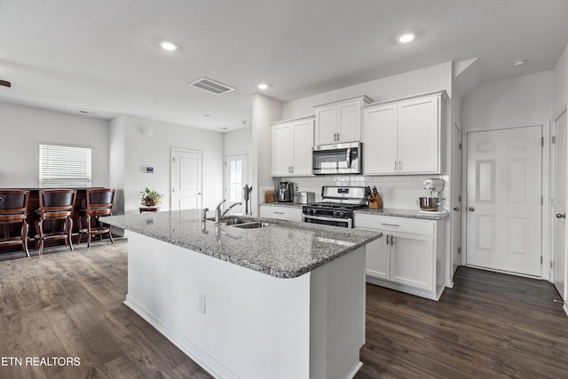 kitchen featuring stainless steel appliances, white cabinetry, light stone countertops, and a center island with sink