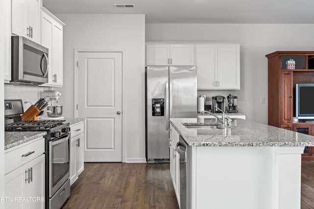 kitchen with sink, appliances with stainless steel finishes, white cabinetry, light stone countertops, and an island with sink