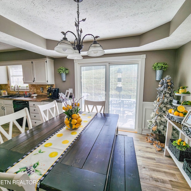 dining area with light hardwood / wood-style floors, sink, a textured ceiling, and a notable chandelier