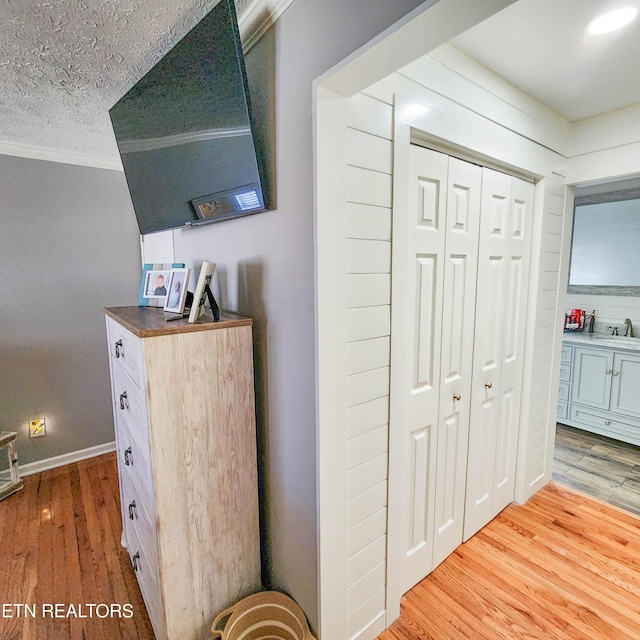 corridor with crown molding, sink, light hardwood / wood-style flooring, and a textured ceiling