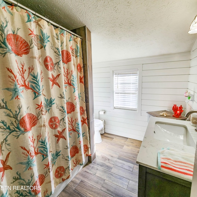 bathroom featuring hardwood / wood-style floors, wooden walls, vanity, walk in shower, and toilet