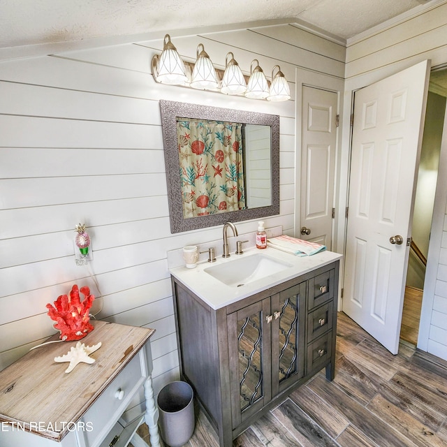 bathroom featuring lofted ceiling, vanity, wood-type flooring, and wood walls