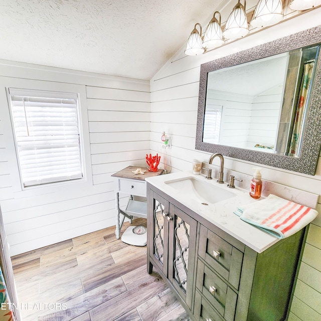 bathroom featuring vanity, vaulted ceiling, a textured ceiling, and wood walls