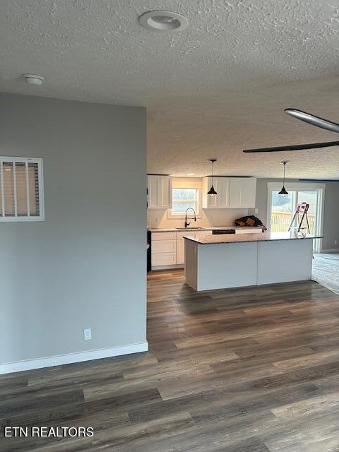 kitchen with a textured ceiling, sink, white cabinetry, and hanging light fixtures