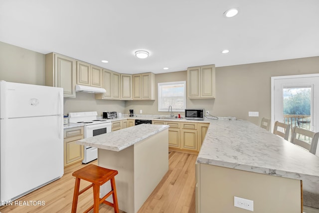 kitchen with a kitchen breakfast bar, white appliances, light hardwood / wood-style floors, and a kitchen island