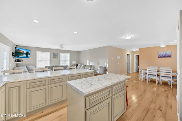 kitchen with a center island, ceiling fan, light stone countertops, cream cabinetry, and light hardwood / wood-style floors