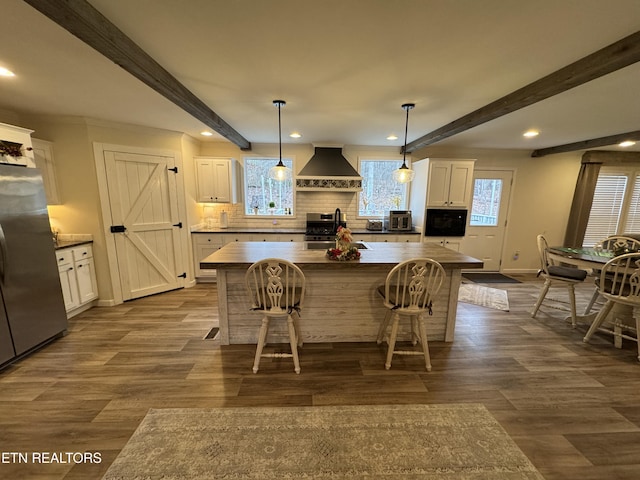 kitchen featuring appliances with stainless steel finishes, wall chimney exhaust hood, a breakfast bar, a center island, and hanging light fixtures