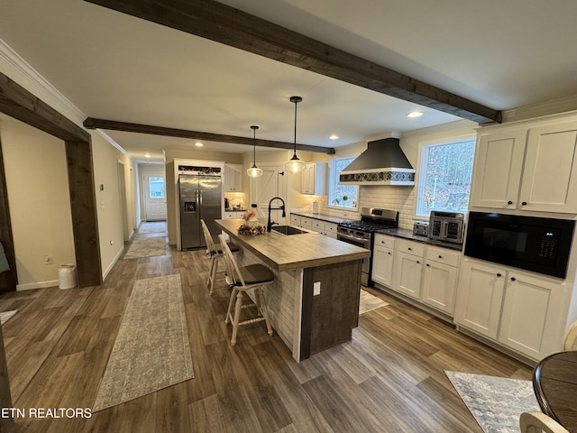 kitchen featuring pendant lighting, a kitchen island with sink, white cabinets, wall chimney exhaust hood, and appliances with stainless steel finishes