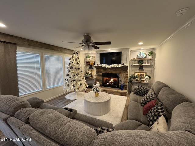 living room featuring hardwood / wood-style floors, ceiling fan, a stone fireplace, and crown molding