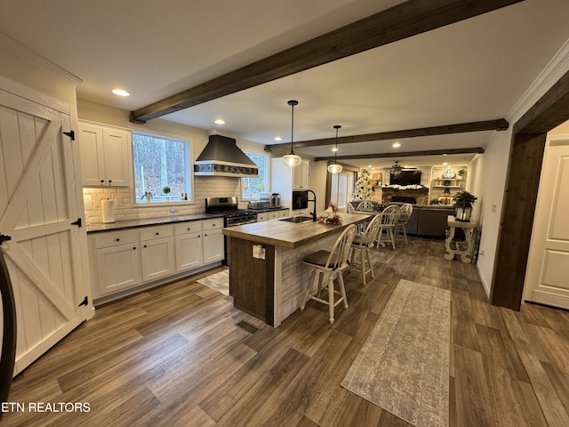 kitchen with pendant lighting, a center island with sink, wall chimney exhaust hood, dark hardwood / wood-style flooring, and white cabinetry