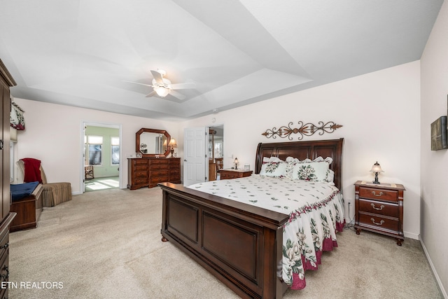 bedroom with ensuite bath, a raised ceiling, ceiling fan, and light colored carpet