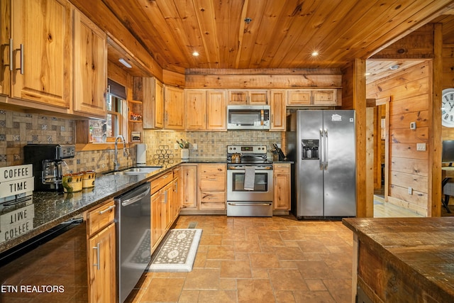 kitchen with wood walls, dark stone counters, sink, appliances with stainless steel finishes, and wood ceiling