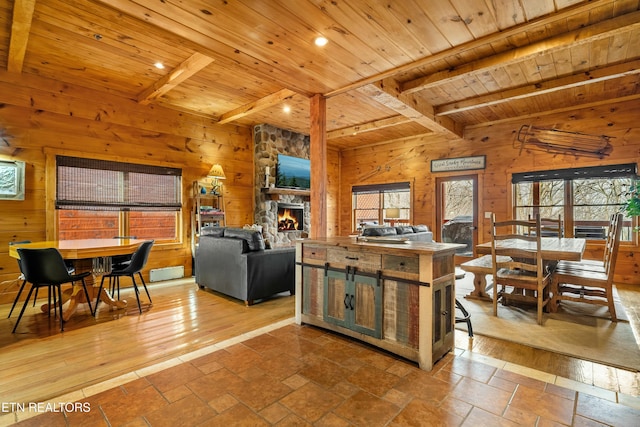 living room with beam ceiling, a stone fireplace, wooden walls, and wood ceiling