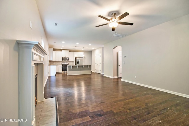 unfurnished living room with a tiled fireplace, ceiling fan, and dark wood-type flooring