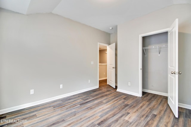 unfurnished bedroom featuring lofted ceiling, a closet, and dark hardwood / wood-style floors