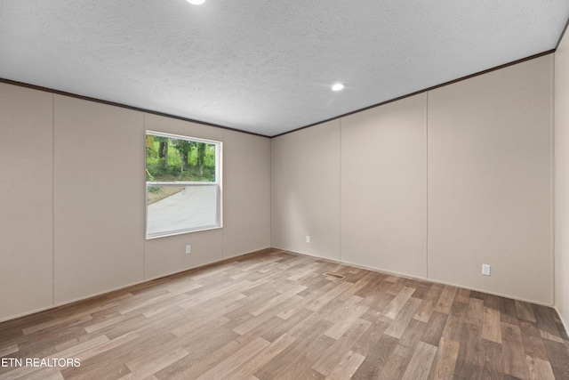 empty room with a textured ceiling, light wood-type flooring, and ornamental molding