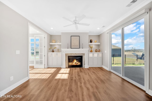 unfurnished living room featuring ceiling fan, built in features, ornamental molding, and light wood-type flooring