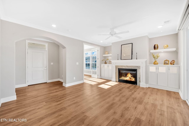 unfurnished living room featuring a premium fireplace, ceiling fan, ornamental molding, and light wood-type flooring