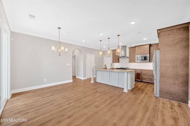 kitchen with stainless steel microwave, wall chimney exhaust hood, white fridge, decorative light fixtures, and a kitchen island with sink