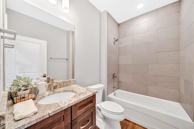 full bathroom with hardwood / wood-style floors, vanity, tiled shower / bath combo, and toilet