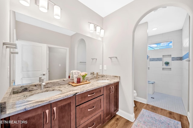 bathroom with toilet, a tile shower, wood-type flooring, and vanity