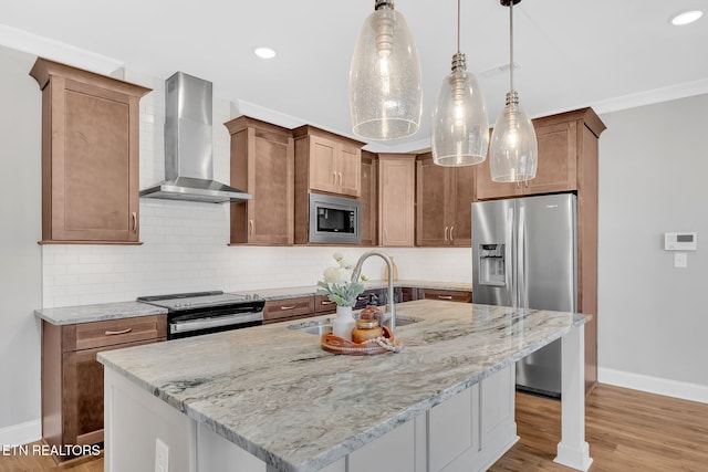 kitchen with stainless steel appliances, a kitchen island with sink, sink, wall chimney range hood, and hanging light fixtures