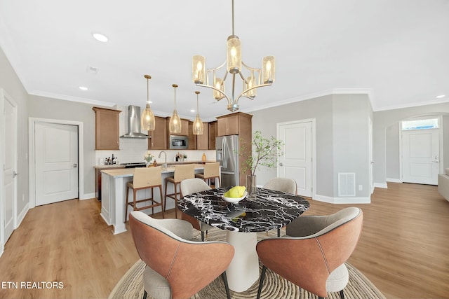 dining space featuring baseboards, light wood finished floors, visible vents, and crown molding