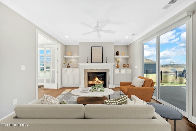 living area with wood finished floors, visible vents, a ceiling fan, a high end fireplace, and baseboards