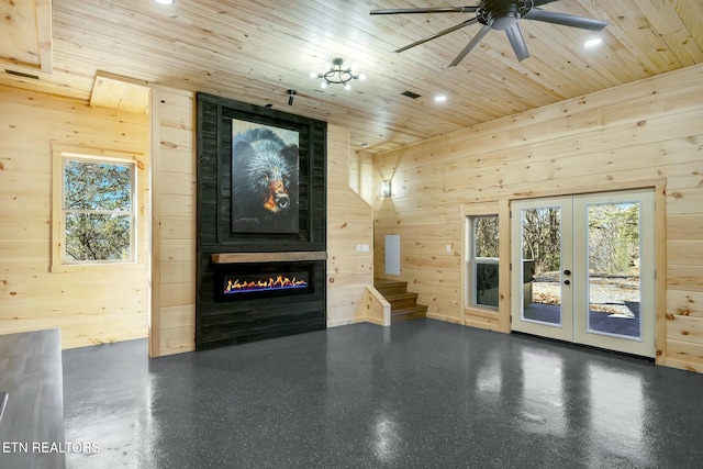 unfurnished living room with ceiling fan, french doors, wooden walls, a fireplace, and wood ceiling