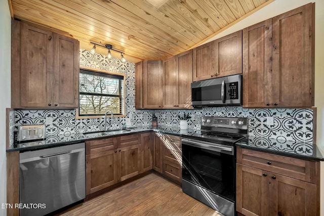 kitchen with sink, dark stone countertops, light hardwood / wood-style floors, wood ceiling, and stainless steel appliances