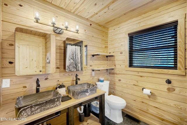 bathroom featuring double sink, wooden walls, wooden ceiling, and toilet