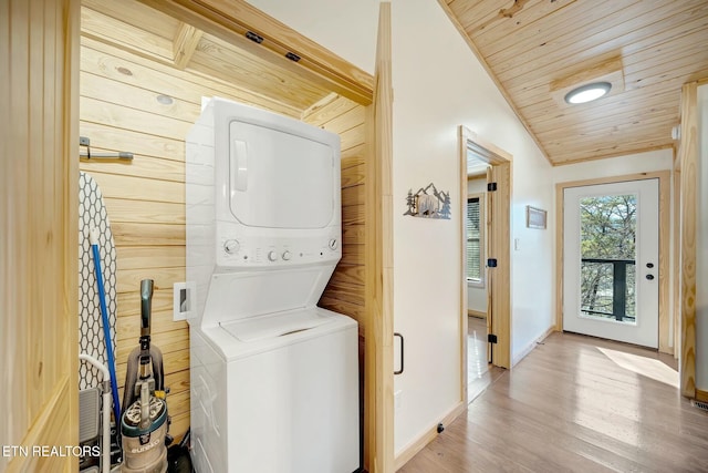 laundry room featuring wood walls, light wood-type flooring, stacked washing maching and dryer, and wood ceiling