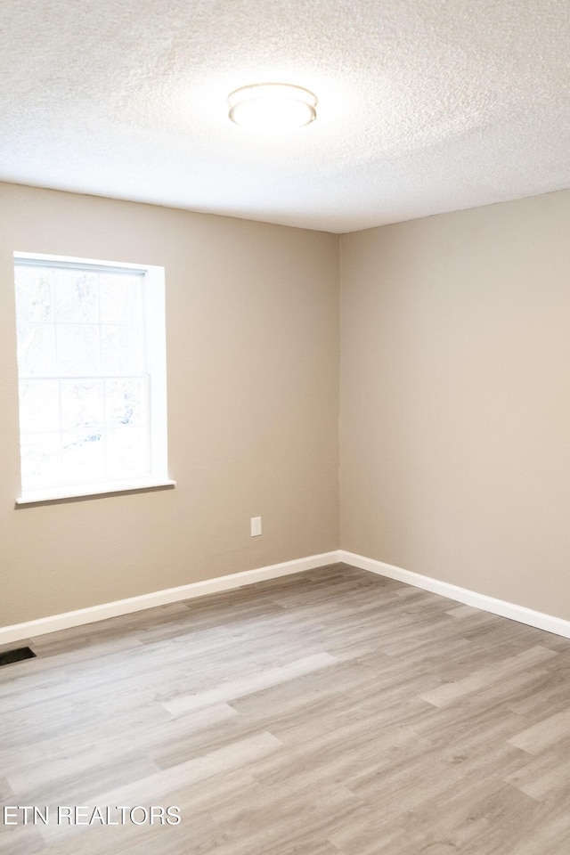 spare room featuring a textured ceiling and light hardwood / wood-style floors