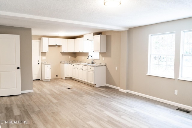 kitchen with white cabinets, sink, light hardwood / wood-style flooring, light stone countertops, and a textured ceiling