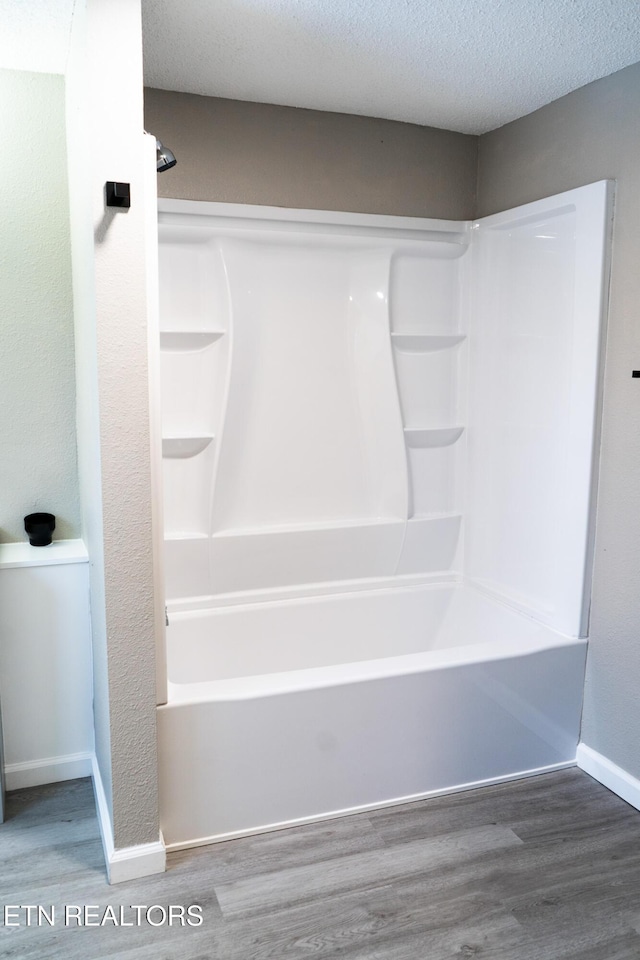 bathroom featuring shower / washtub combination, wood-type flooring, and a textured ceiling