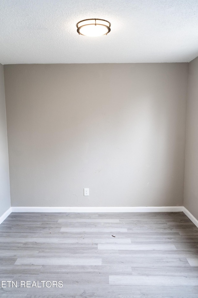 unfurnished room with a textured ceiling, baseboards, and wood finished floors