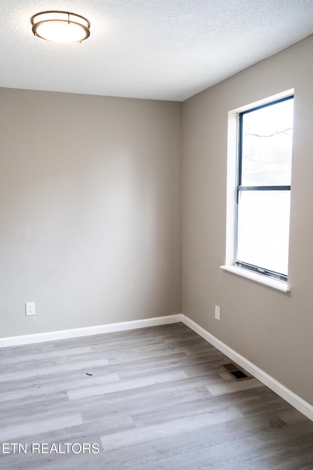 empty room featuring visible vents, a textured ceiling, baseboards, and wood finished floors