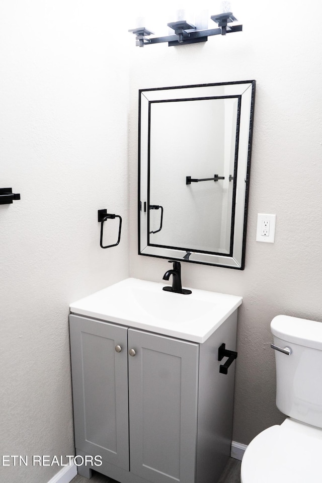 half bathroom with toilet, vanity, and baseboards