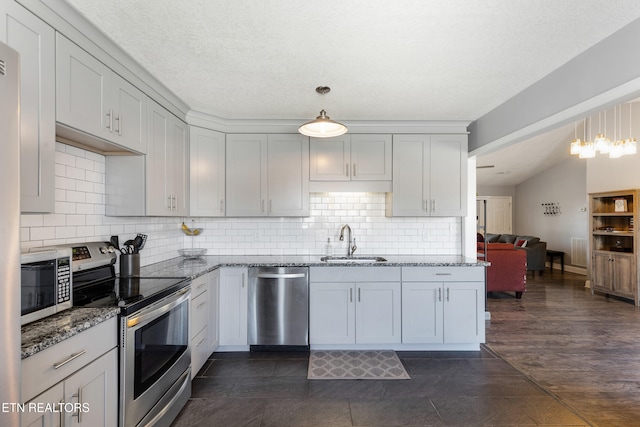 kitchen with stone countertops, appliances with stainless steel finishes, decorative light fixtures, sink, and decorative backsplash