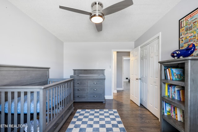 unfurnished bedroom featuring a textured ceiling, dark hardwood / wood-style flooring, a closet, a crib, and ceiling fan