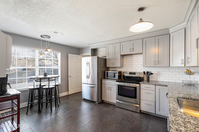 kitchen featuring light stone countertops, pendant lighting, appliances with stainless steel finishes, a textured ceiling, and tasteful backsplash