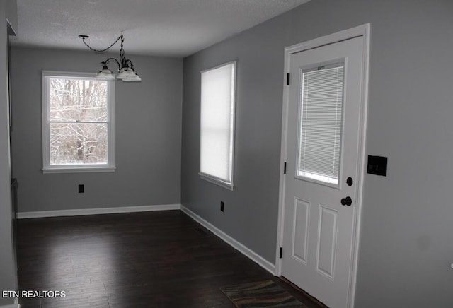 unfurnished dining area with dark hardwood / wood-style floors, a textured ceiling, and a chandelier