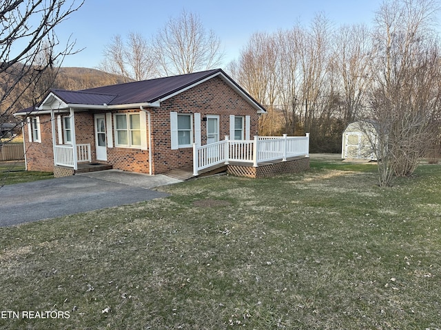 view of front facade featuring a front yard, an outdoor structure, aphalt driveway, brick siding, and metal roof