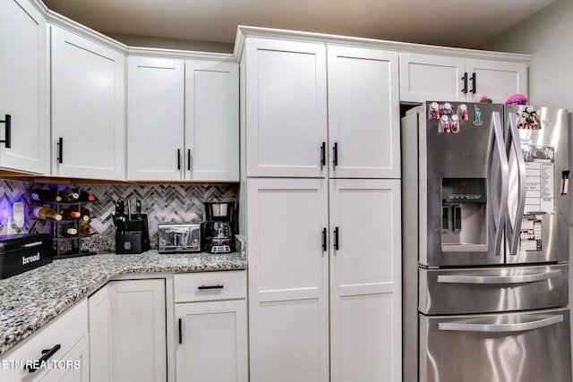 kitchen with white cabinets, decorative backsplash, stainless steel fridge, and light stone counters