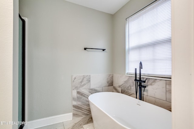 bathroom featuring tile patterned floors, a washtub, a healthy amount of sunlight, and tile walls