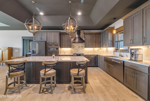 kitchen with a center island, pendant lighting, wall chimney range hood, and appliances with stainless steel finishes