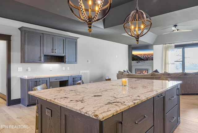 kitchen featuring light stone countertops, dark brown cabinets, ceiling fan with notable chandelier, and light hardwood / wood-style floors