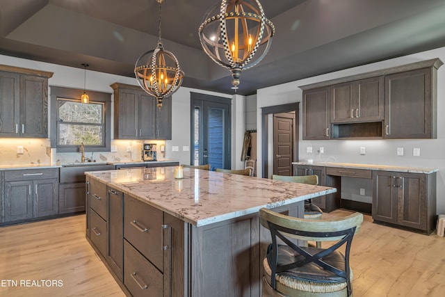 kitchen featuring pendant lighting, an inviting chandelier, light stone countertops, a tray ceiling, and a kitchen island